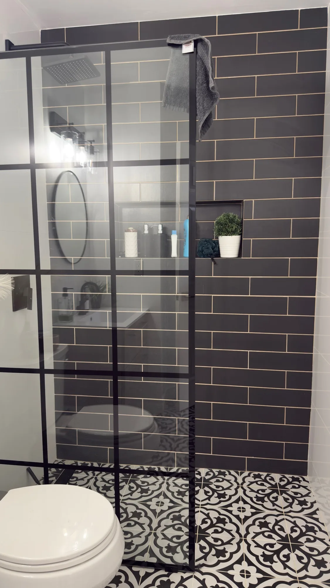 Black subway tile shower with black-grid frameless glass screen and encaustic floor tile — D&D Interior Services
