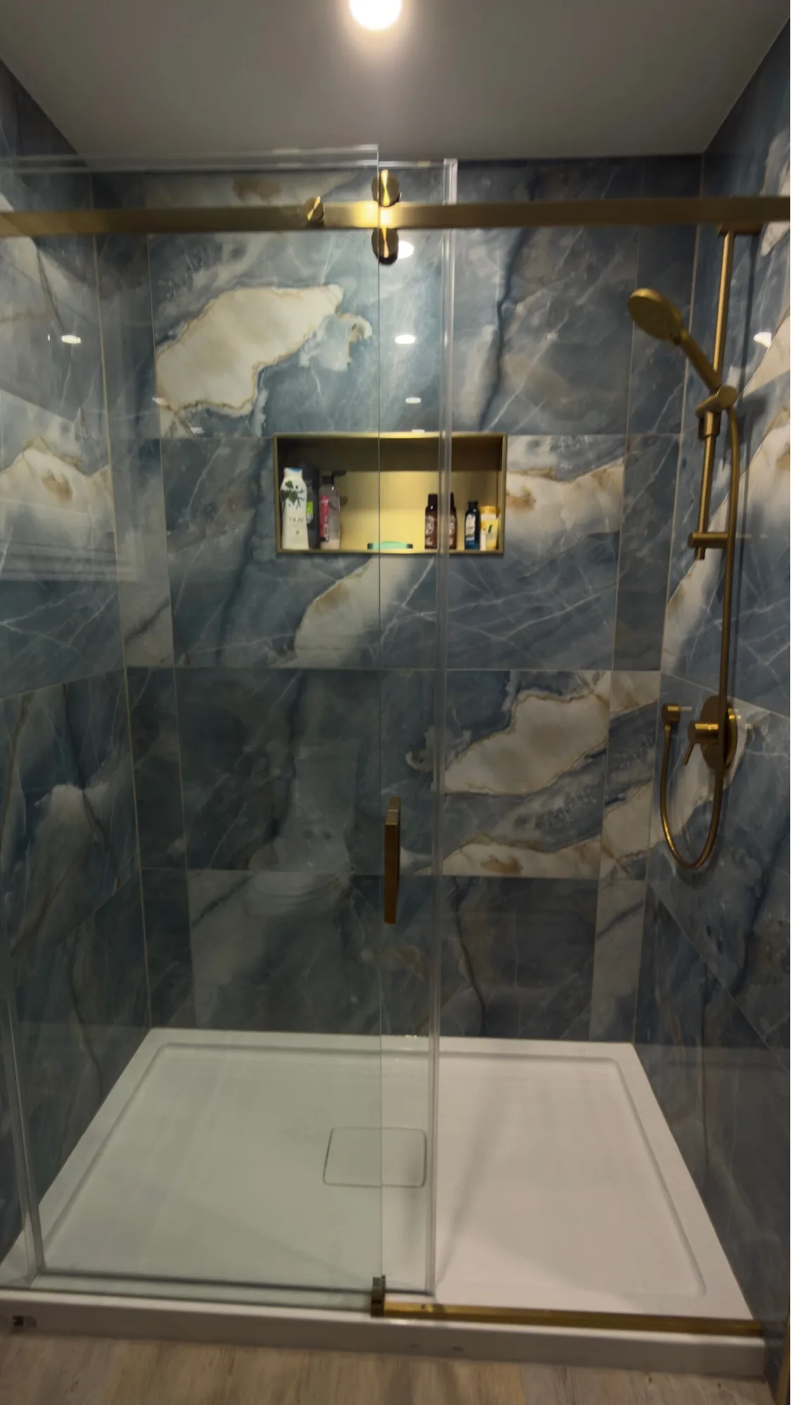 Blue onyx walk-in shower with gold sliding glass door hardware and rainfall fixture — D&D Interior Services