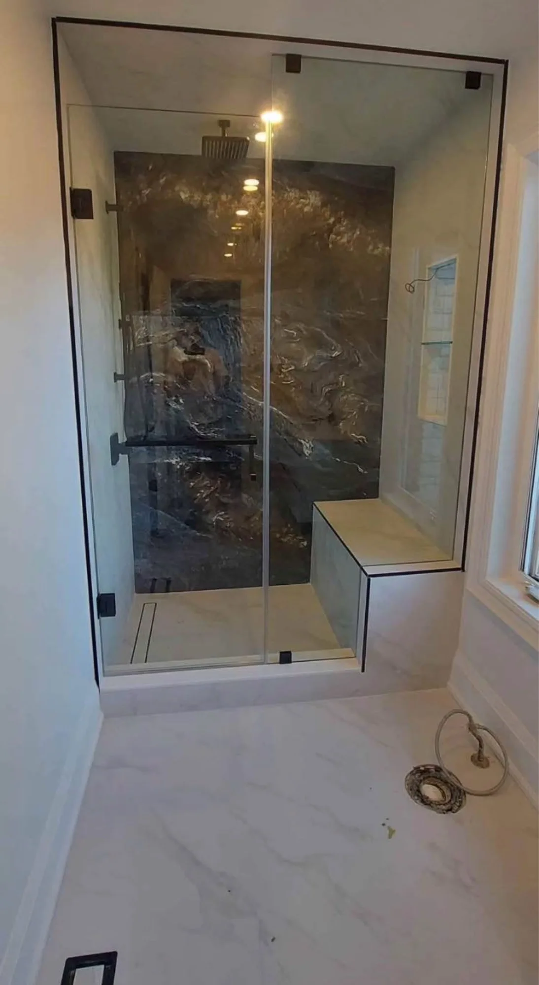 Dramatic dark marble feature wall walk-in shower with frameless glass enclosure, rain head, integrated bench seat, and linear drain — D&D Interior Services Kitchener