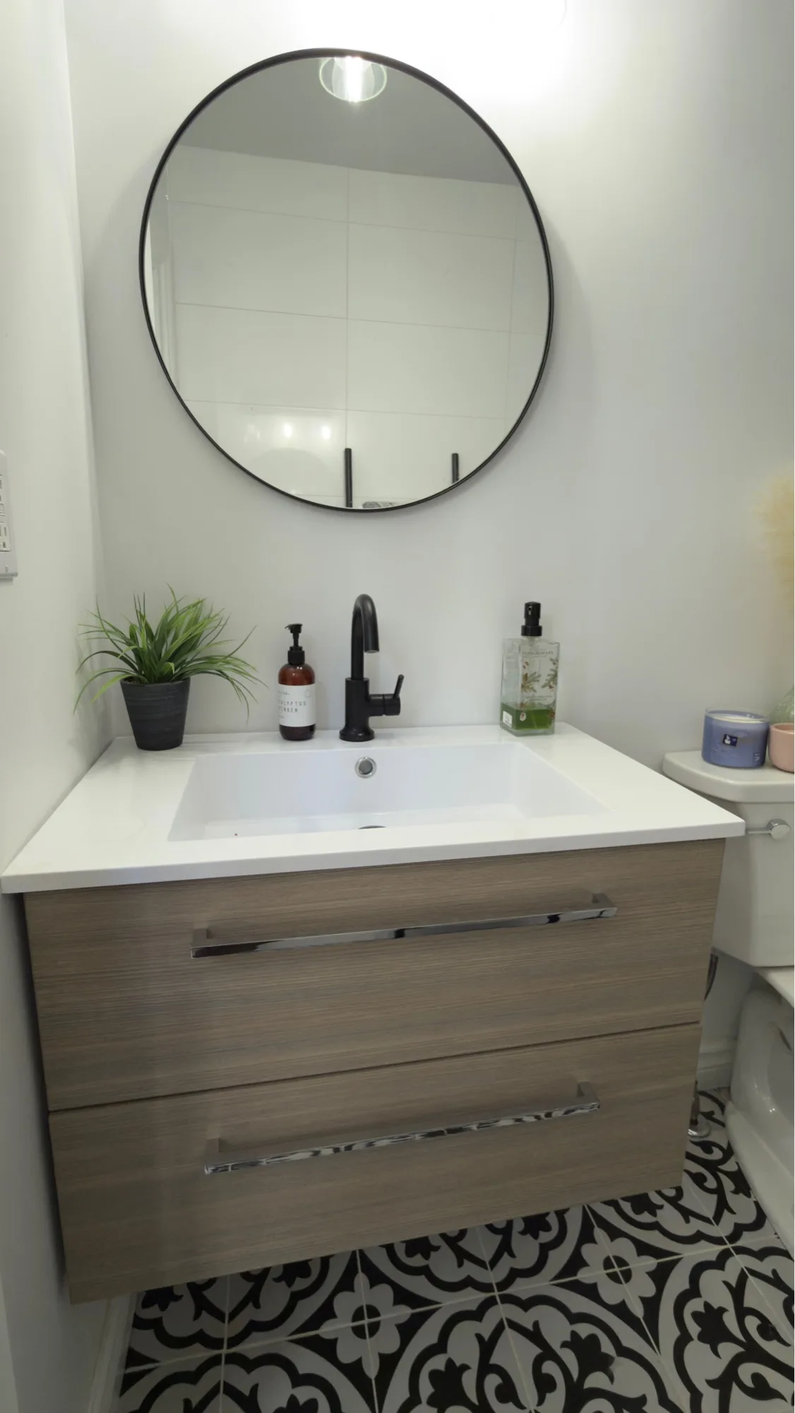 Powder room with floating wood-look vanity, round black-frame mirror and encaustic floor tile — D&D Interior Services