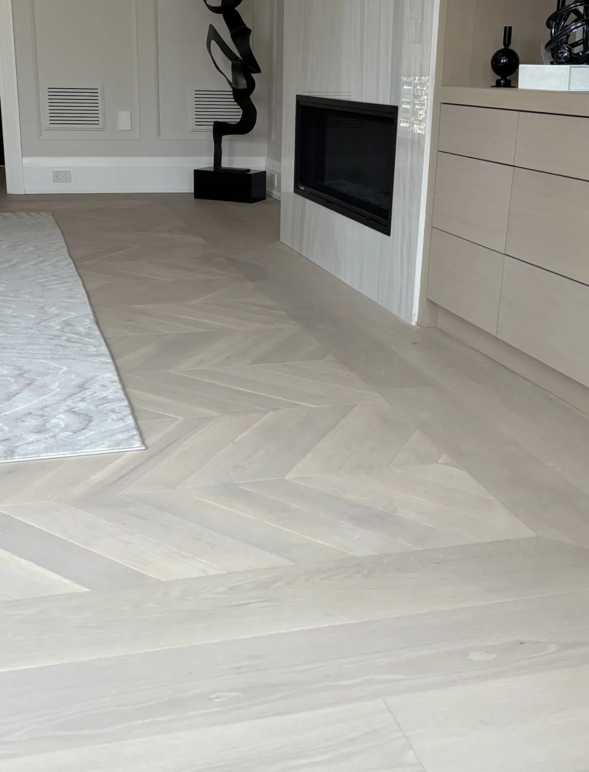 Pale herringbone floor meeting a fireplace wall and white built-in storage