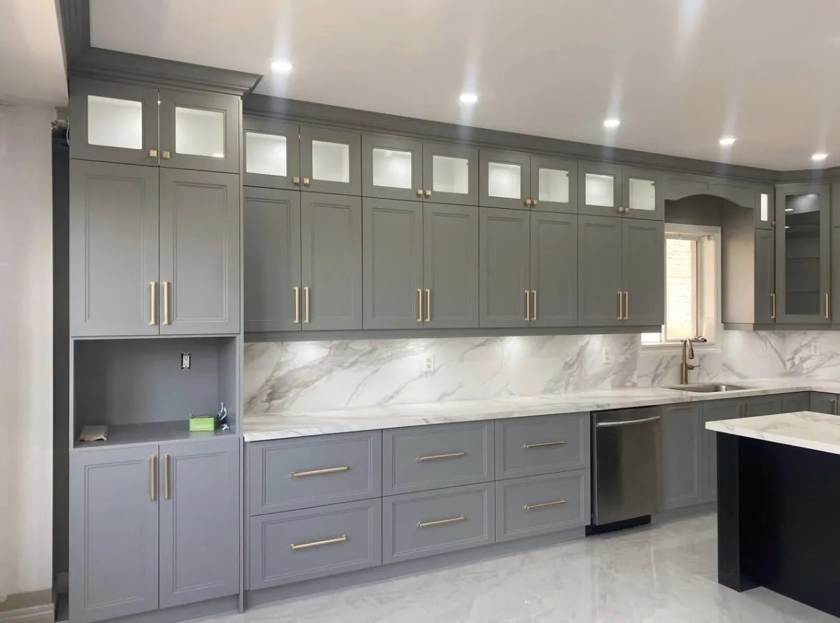 Grey kitchen cabinets with dark handles, glass upper doors and a light worktop