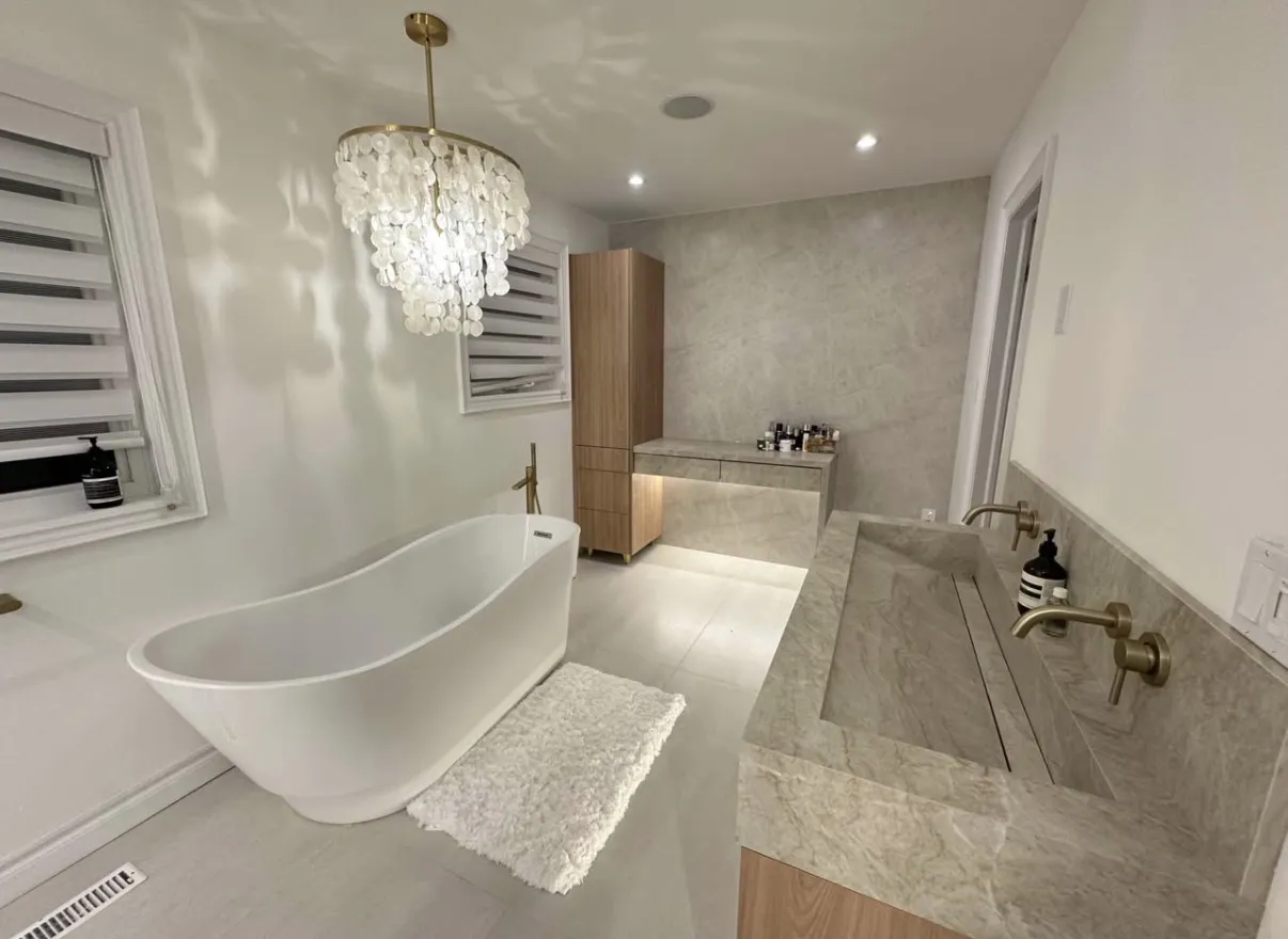 Freestanding white bathtub beside a wood vanity, warm metal taps and a pendant light